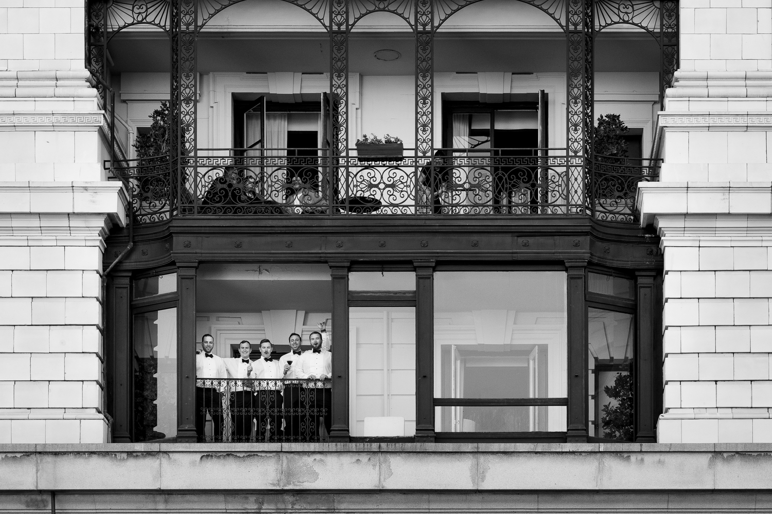 Groomsmen celebrate amongst architectural details of classic building facades with ornate balconies and windows in black and white in SF.