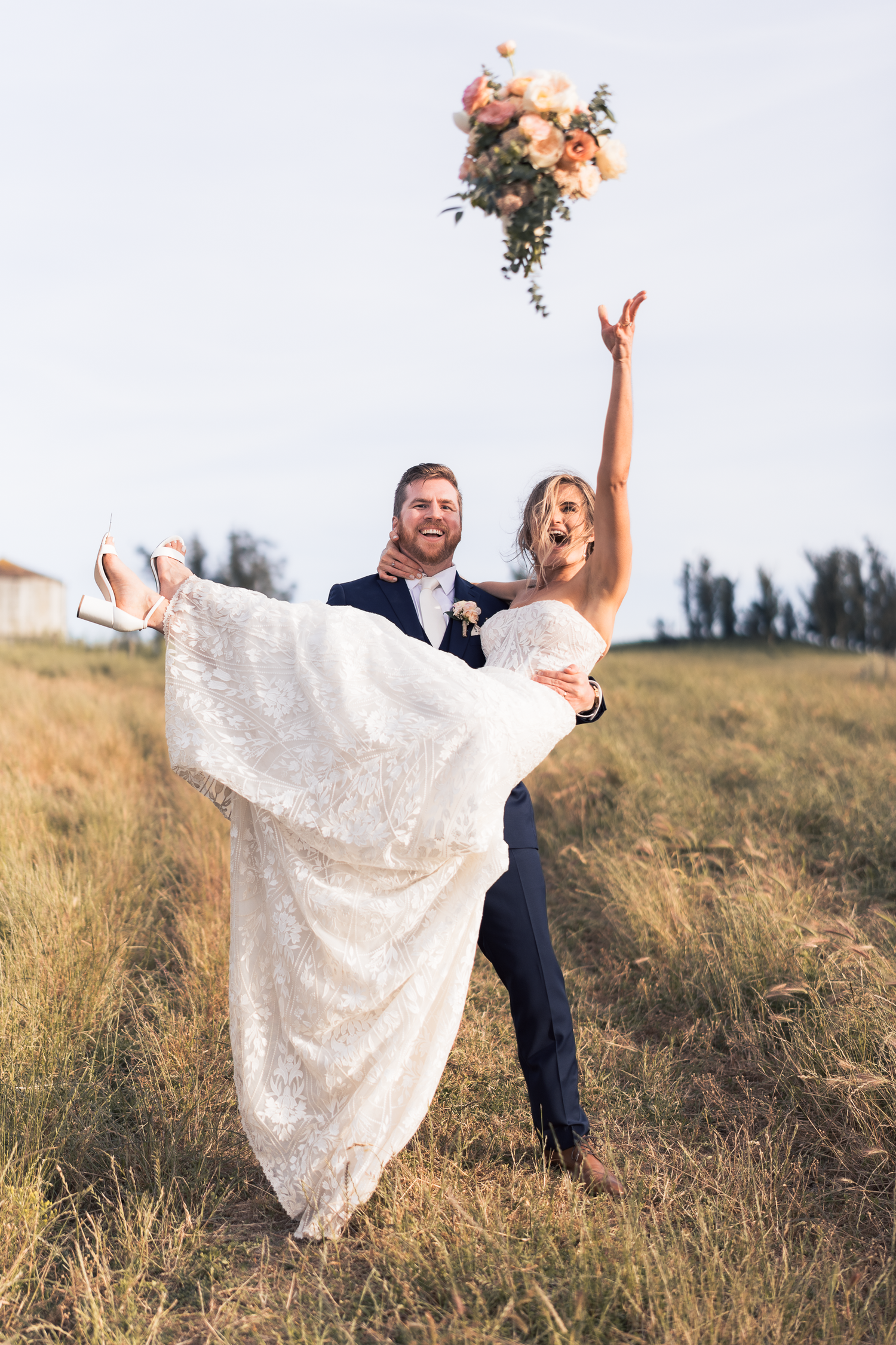 A couple in wedding attire poses playfully in a grassy field during a sunset photoshoot at Olympia's Valley Estate in Petaluma.