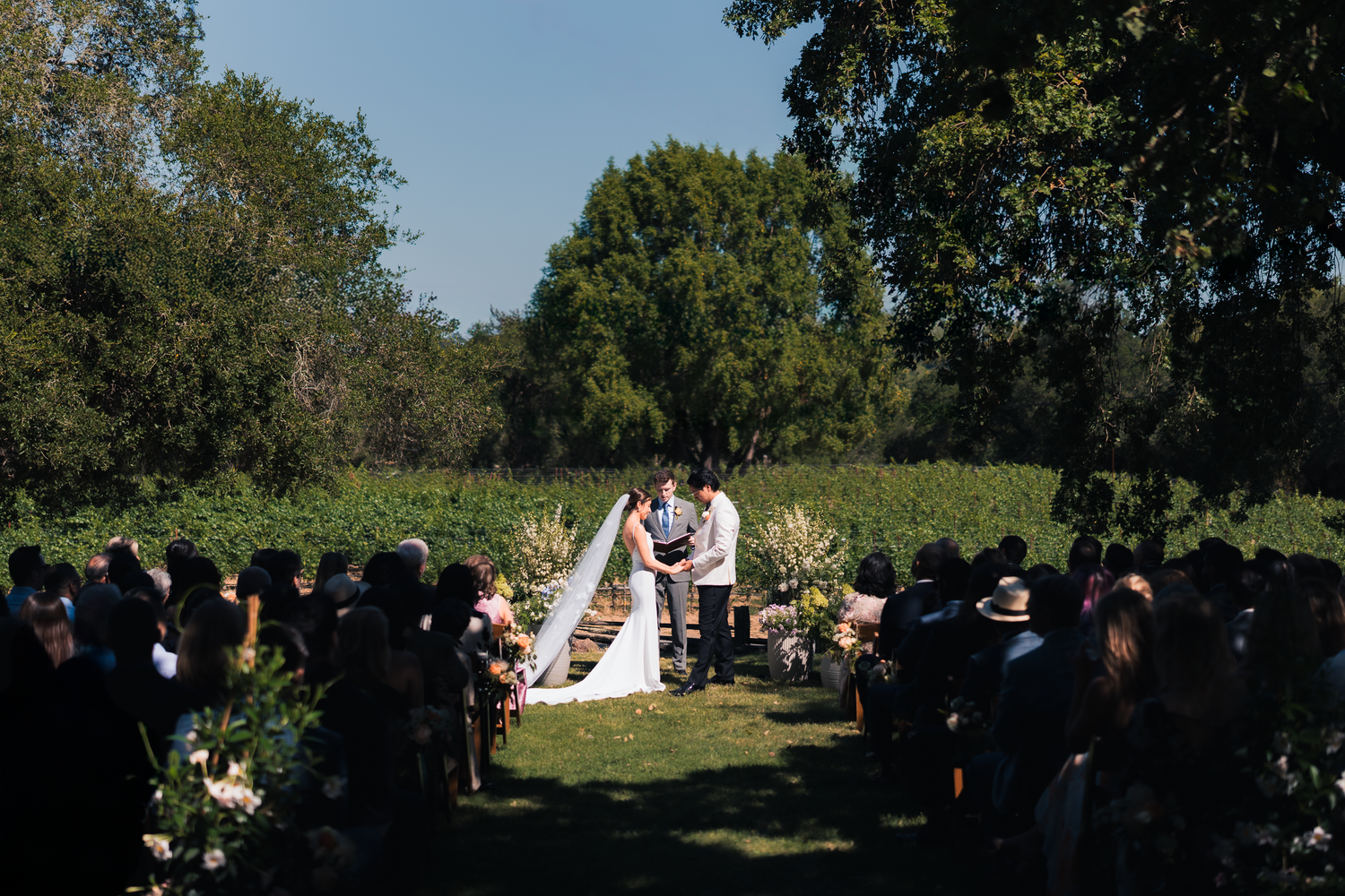 Wide angle view of an outdoor wedding ceremony with guests seated under trees at Harper's Rest in Healdsburg, California.