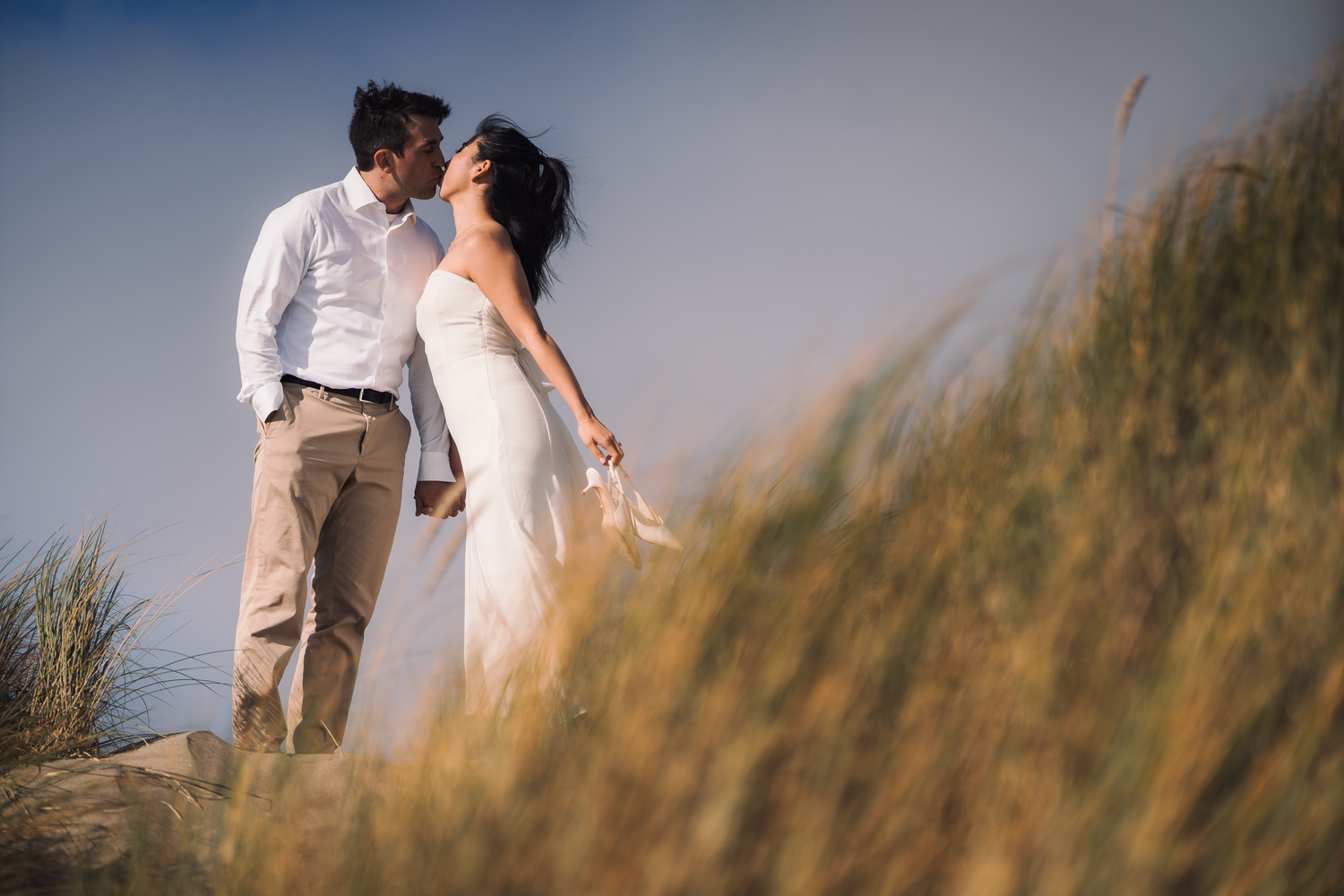 A couple shares an intimate moment among tall beach grass during dusk at Ocean Beach in San Francisco.