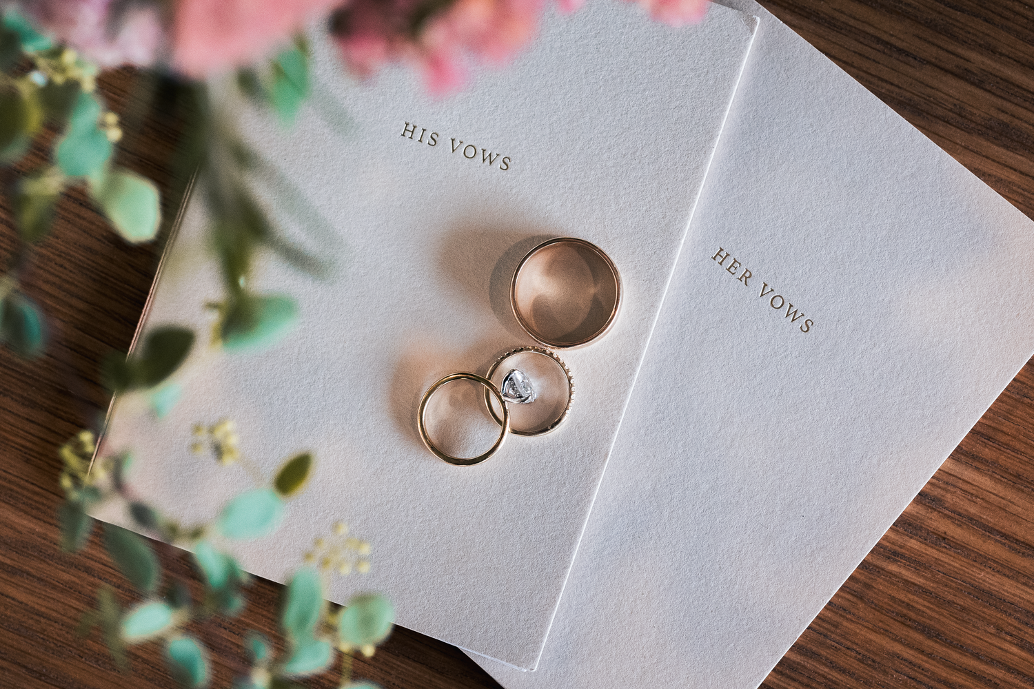 Wedding rings and vow books styled on wooden surface with delicate greenery at Olympia's Valley Estate in Petaluma.