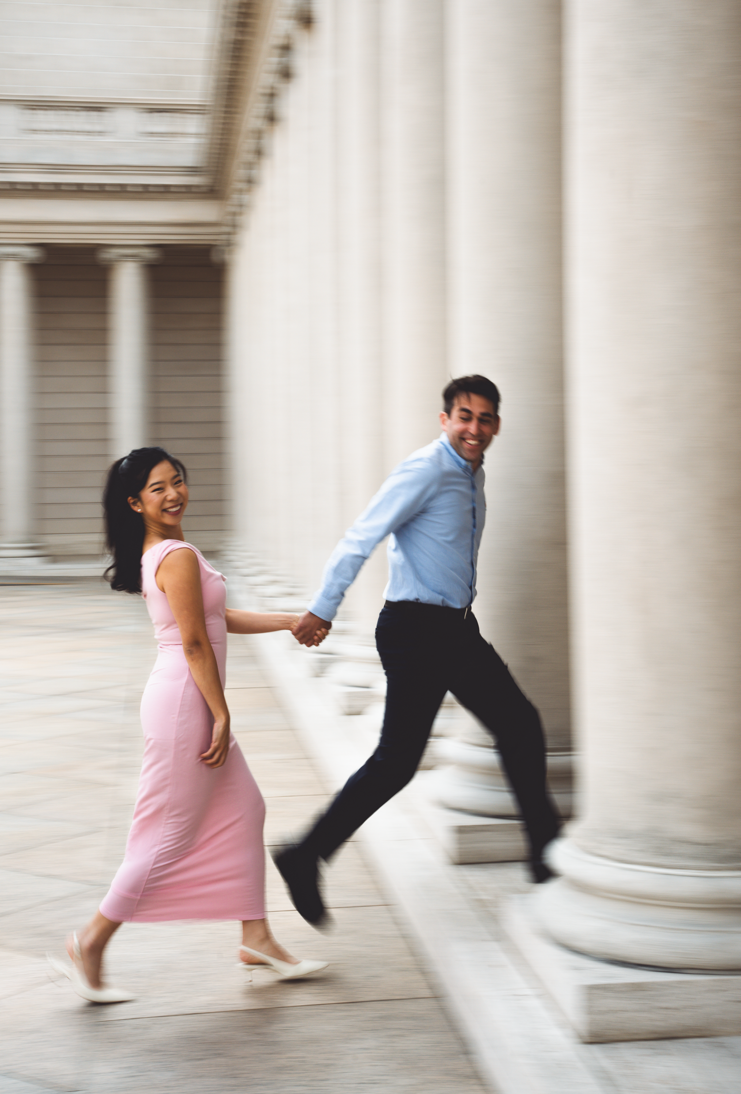 Playful couple running between classical white columns in motion blur at the Legion of Honor in San Francisco, California.