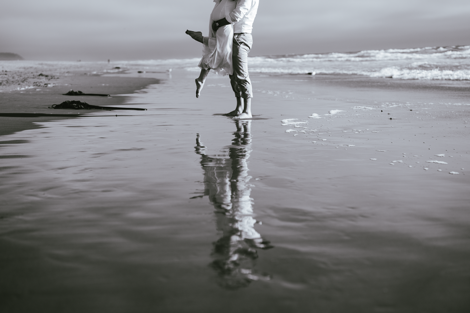 Artistic black and white photo of legs and their reflection walking on wet beach sand at Ocean Beach in San Francisco.