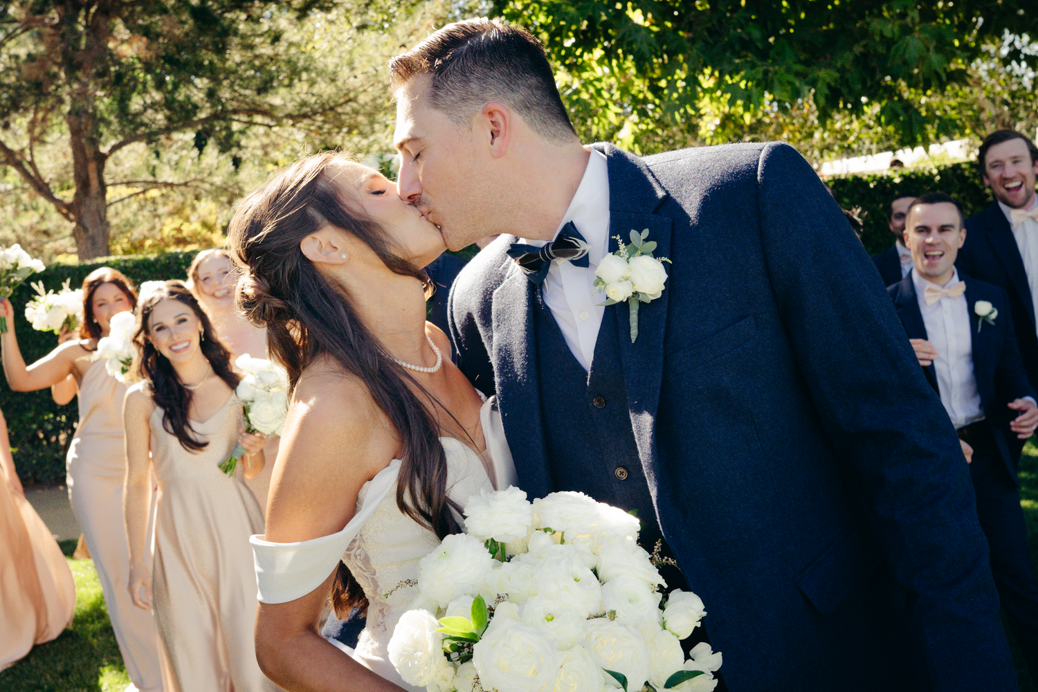 Wedding couple sharing romantic kiss with bridal party in background at Cornerstone Sonoma.