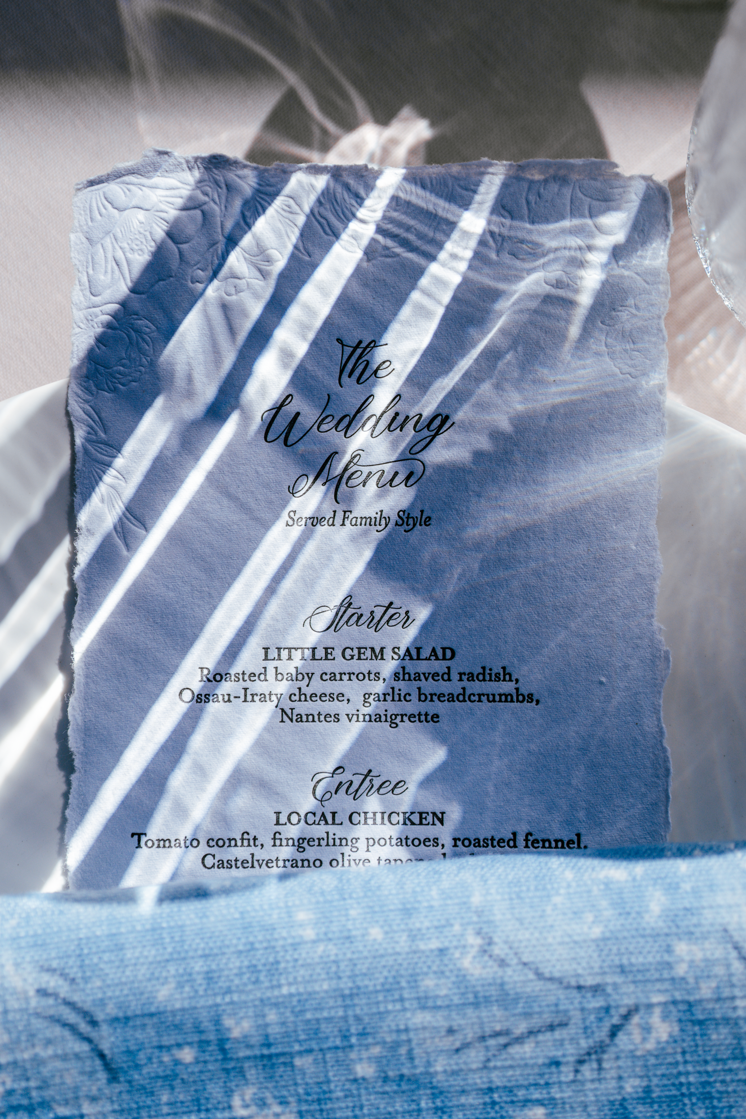 Wedding menu card with elegant script typography photographed with reflection of table settings.