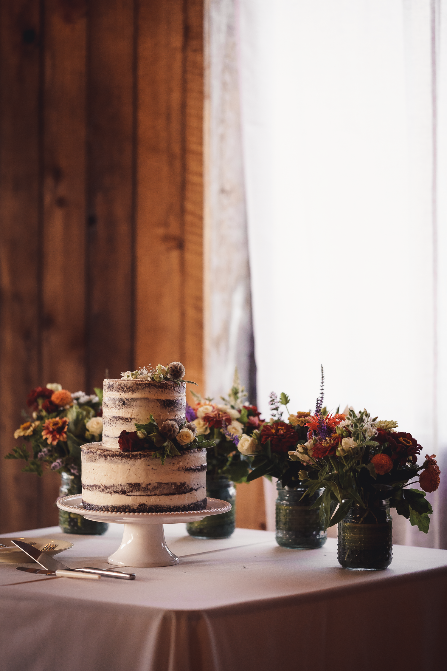 A rustic wedding cake display with fresh flowers and greenery on a white tablecloth at Cow-Track-Ranch in Marin County.