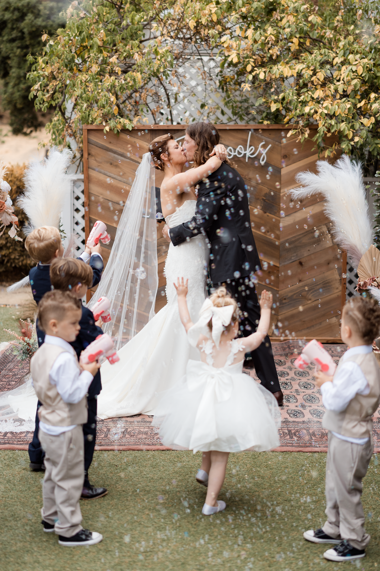 First Kiss during wedding ceremony with flower petals being tossed in a garden setting at Falkirk Mansion in Marin County.