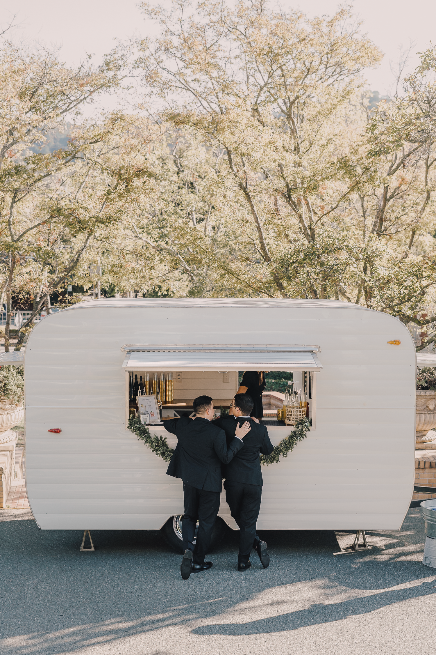 Two people in suits ordering drinks at a vintage white camper trailer that has been turned into a bar. Photographed at Falkirk Mansion.