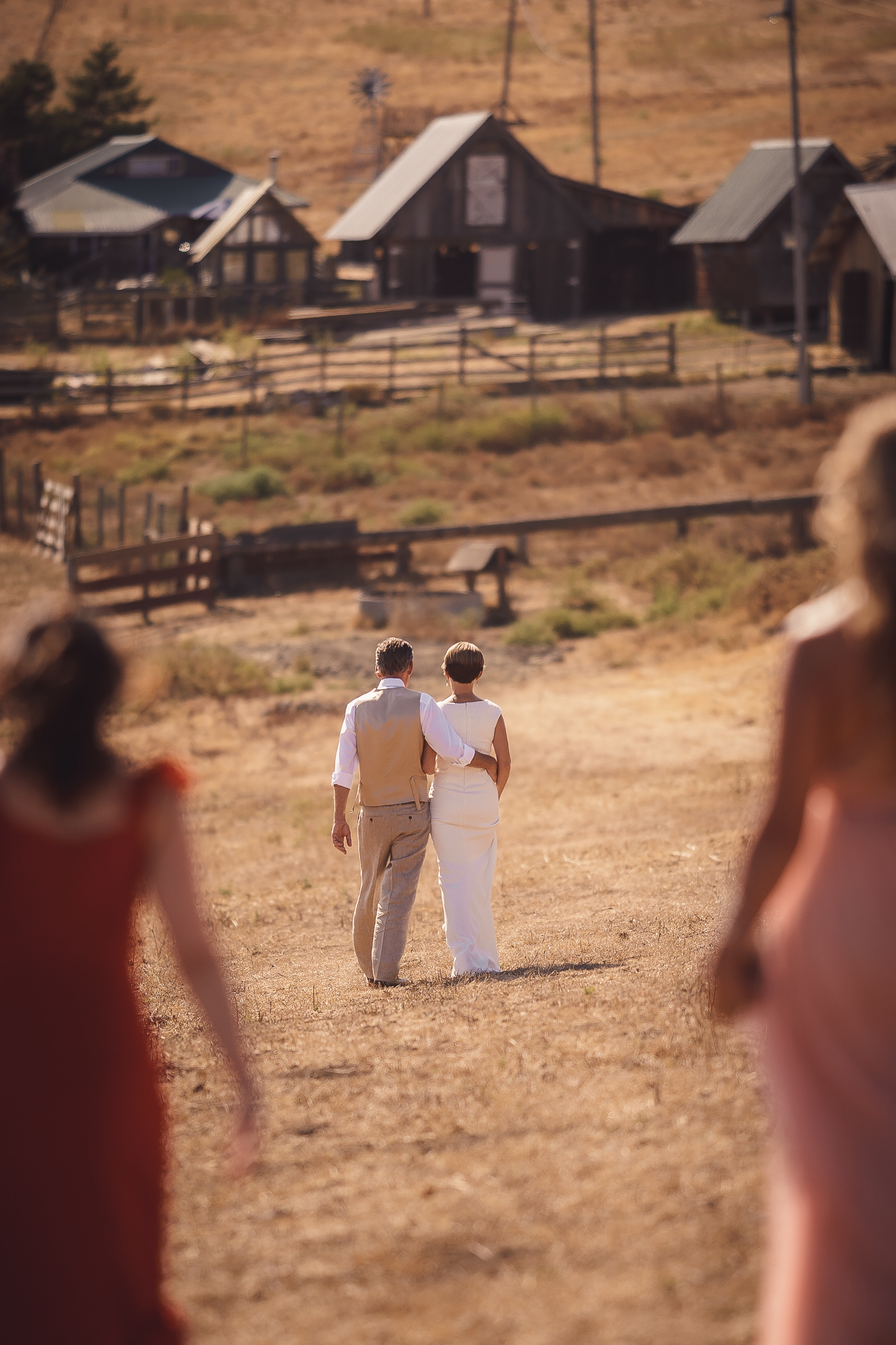 Distant view of a couple walking through a rustic ranch setting with buildings in background at Cow-Track Ranch in Marin County.