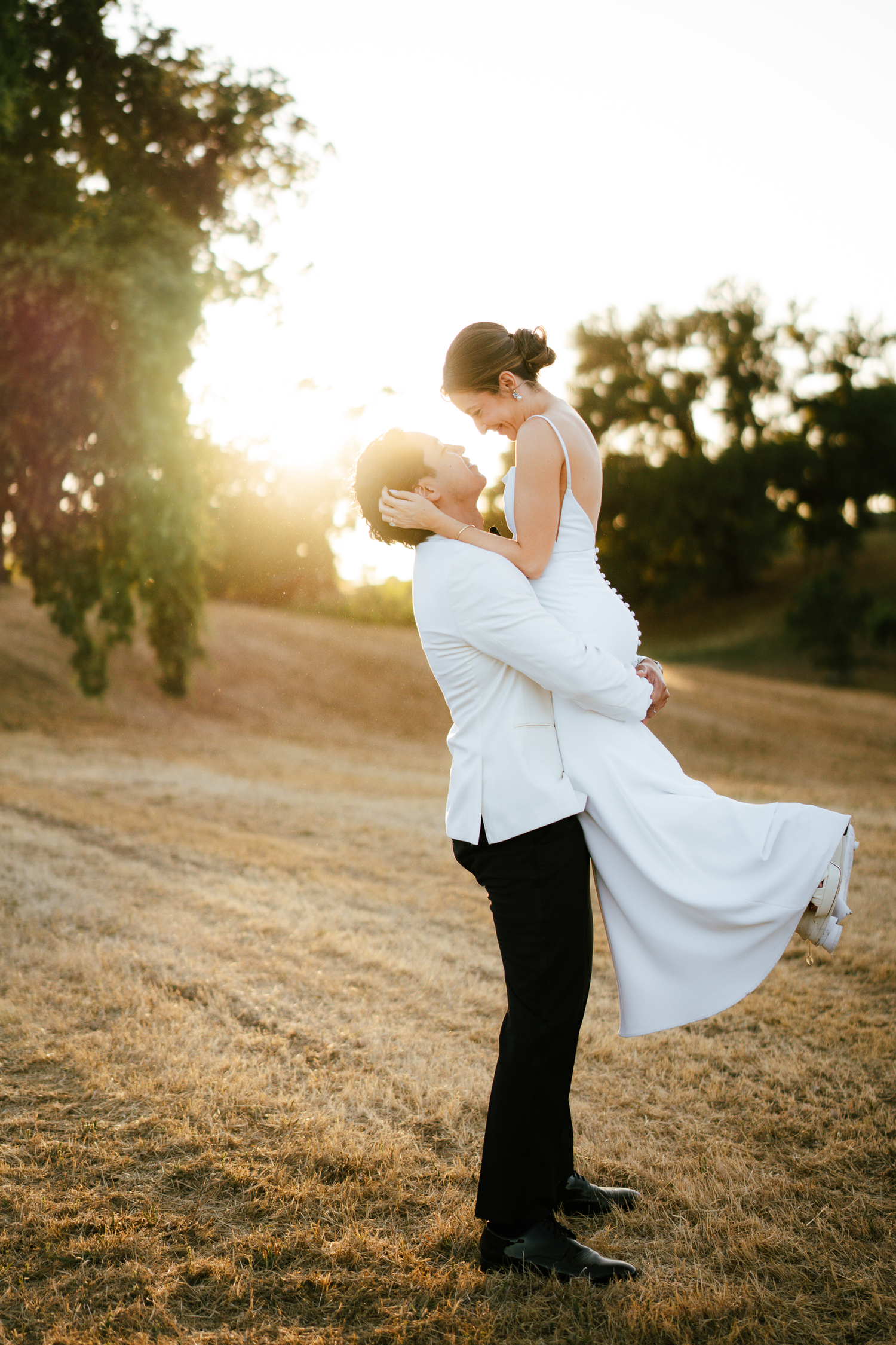 Romantic sunset wedding portrait with groom lifting bride in white dress at Harper's Rest in Healdsburg, California.