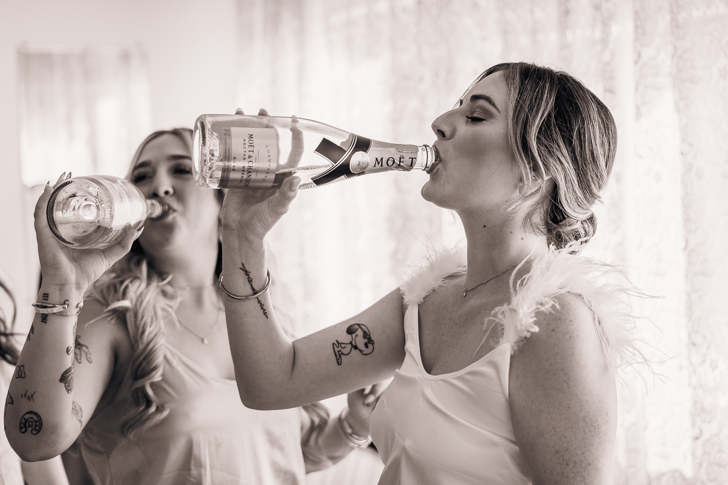 Bride and bridesmaids in formal attire drinking champagne during wedding preparations.