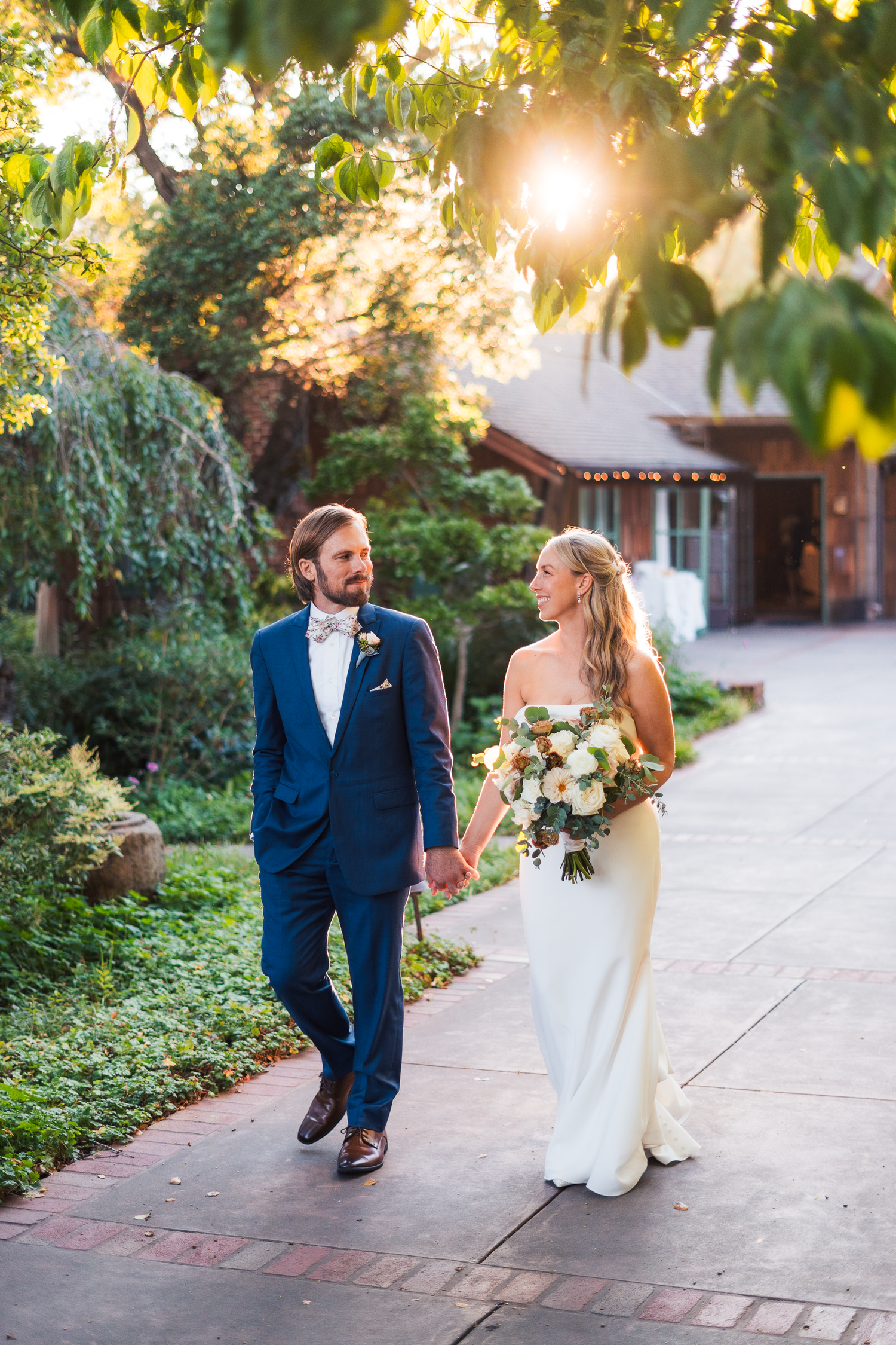 Bride and groom walking hand in hand on garden path during golden hour at the Outdoor Art Club in Mill Valley, California.