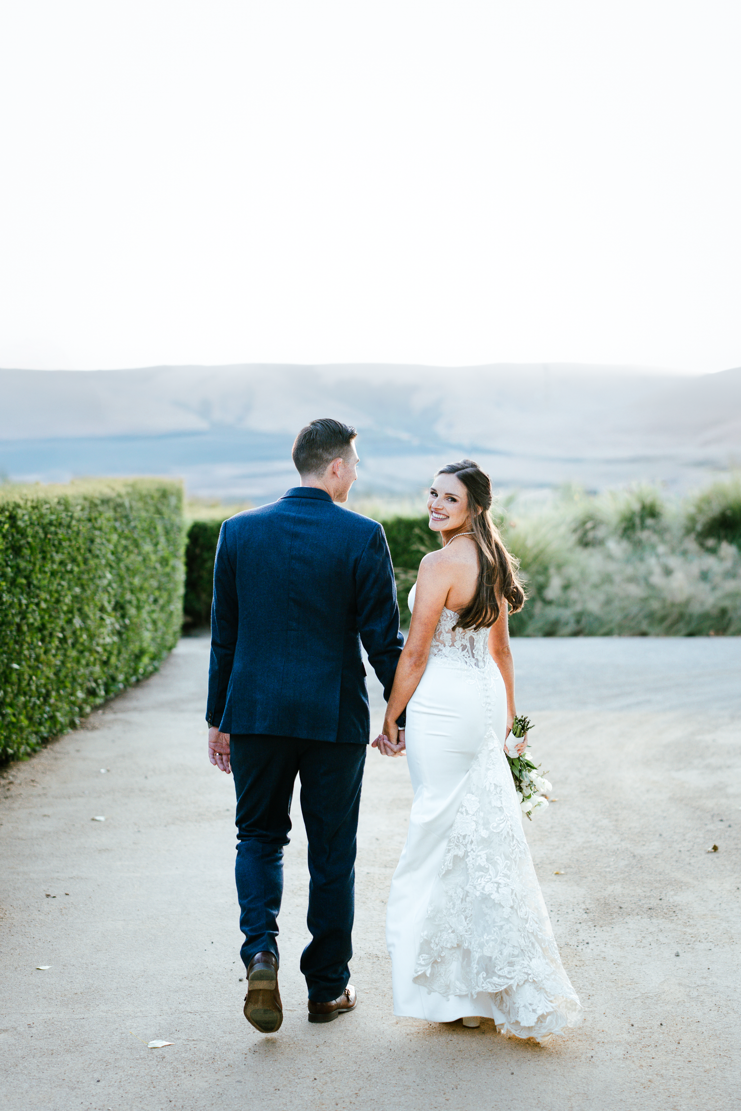 A couple walking hand in hand down a scenic path with mountains in the background at Cornerstone Sonoma.