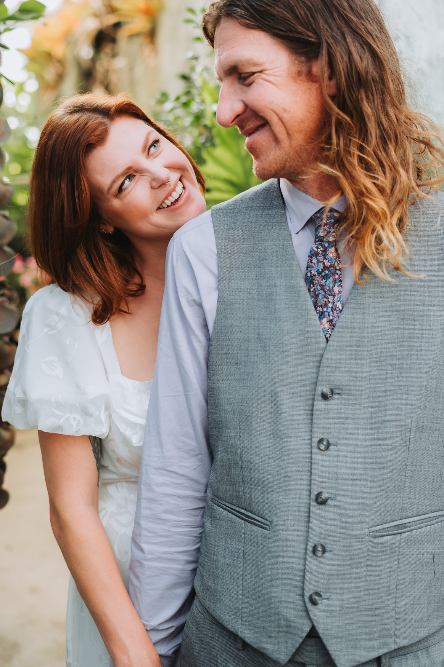 Romantic couple portrait during engagement photoshoot with one wearing a grey vest in a garden setting at Shelldance Orchid Farm in Pacifica