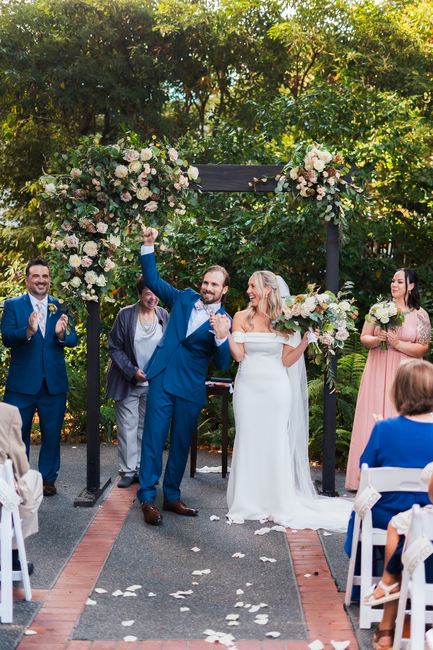 Bride and groom celebrate after wedding ceremony with white chairs and floral arch in a garden setting at Outdoor Art Club in Mill Valley.