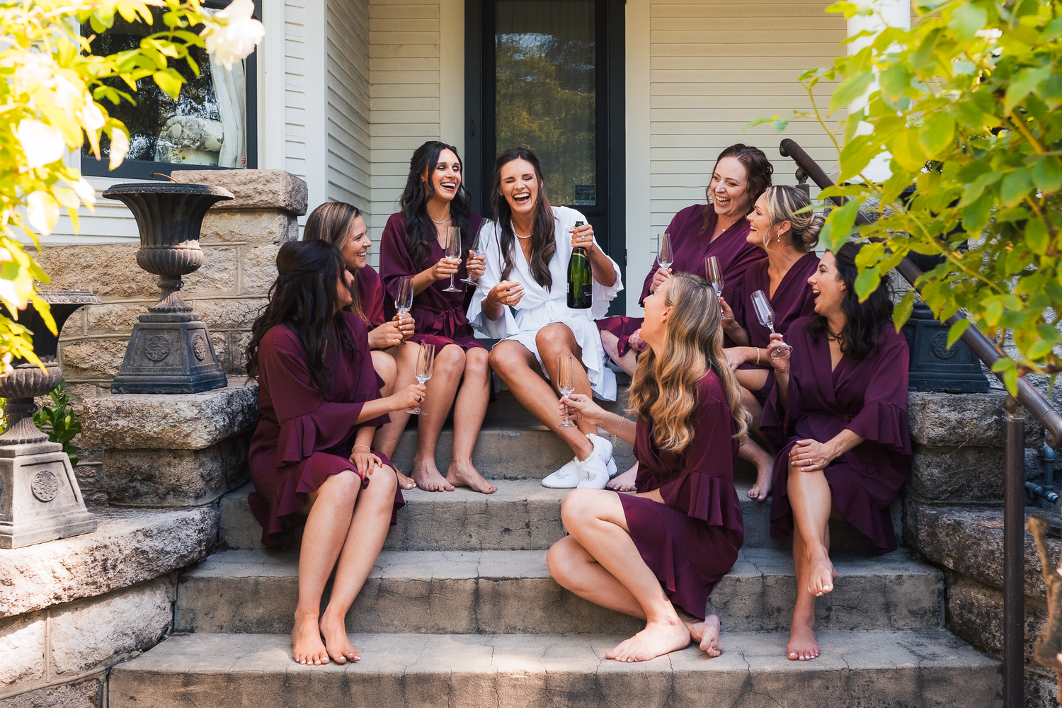 Bridesmaids in burgundy dresses sitting together on stone steps outdoors in Sonoma County.