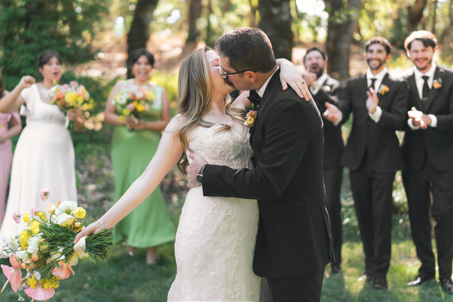 Wedding party celebrating outdoors with joyful reactions in a sunlit garden setting at Yokayo Ranch in Ukiah.