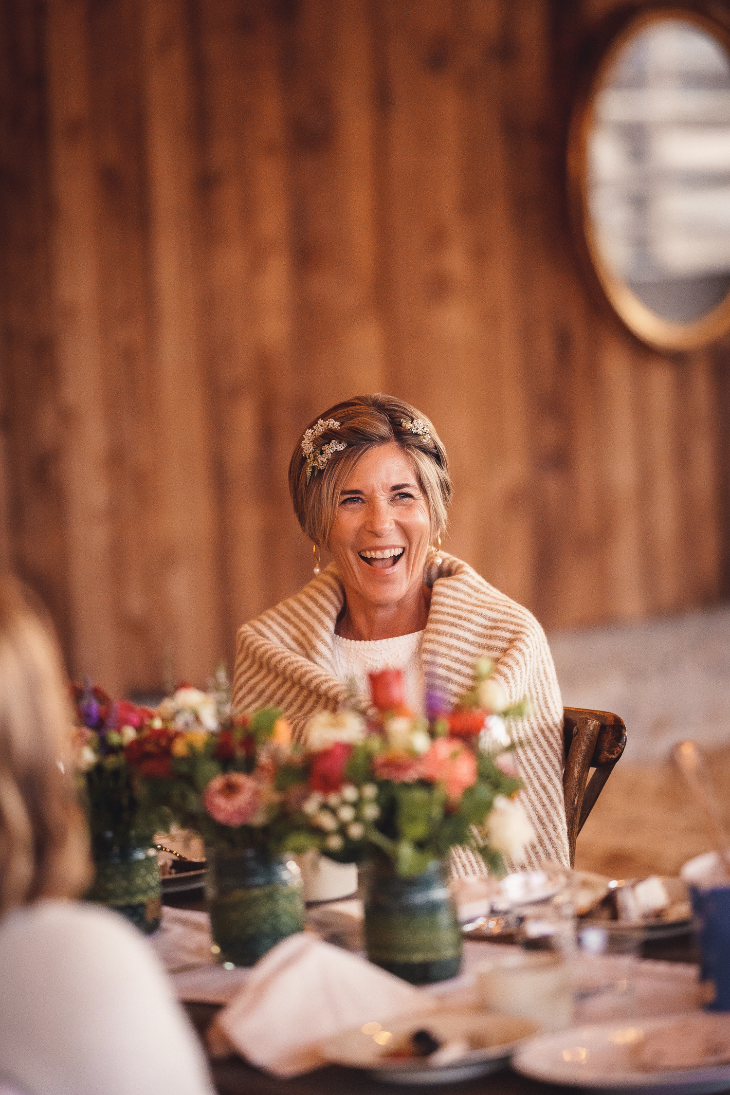 Bride smiling during reception dinner, with rustic floral arrangements on table in a rustic barn at Cow-Track Ranch in Marin County.