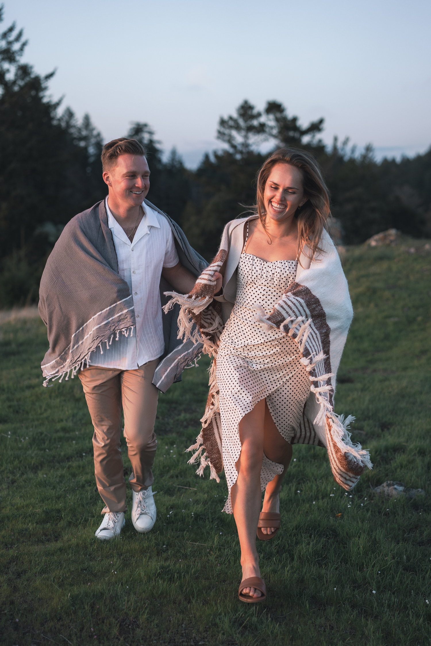 Playful couple runs through grassy field at dusk wearing white and beige outfits on Mount Tamalpais in Marin County.
