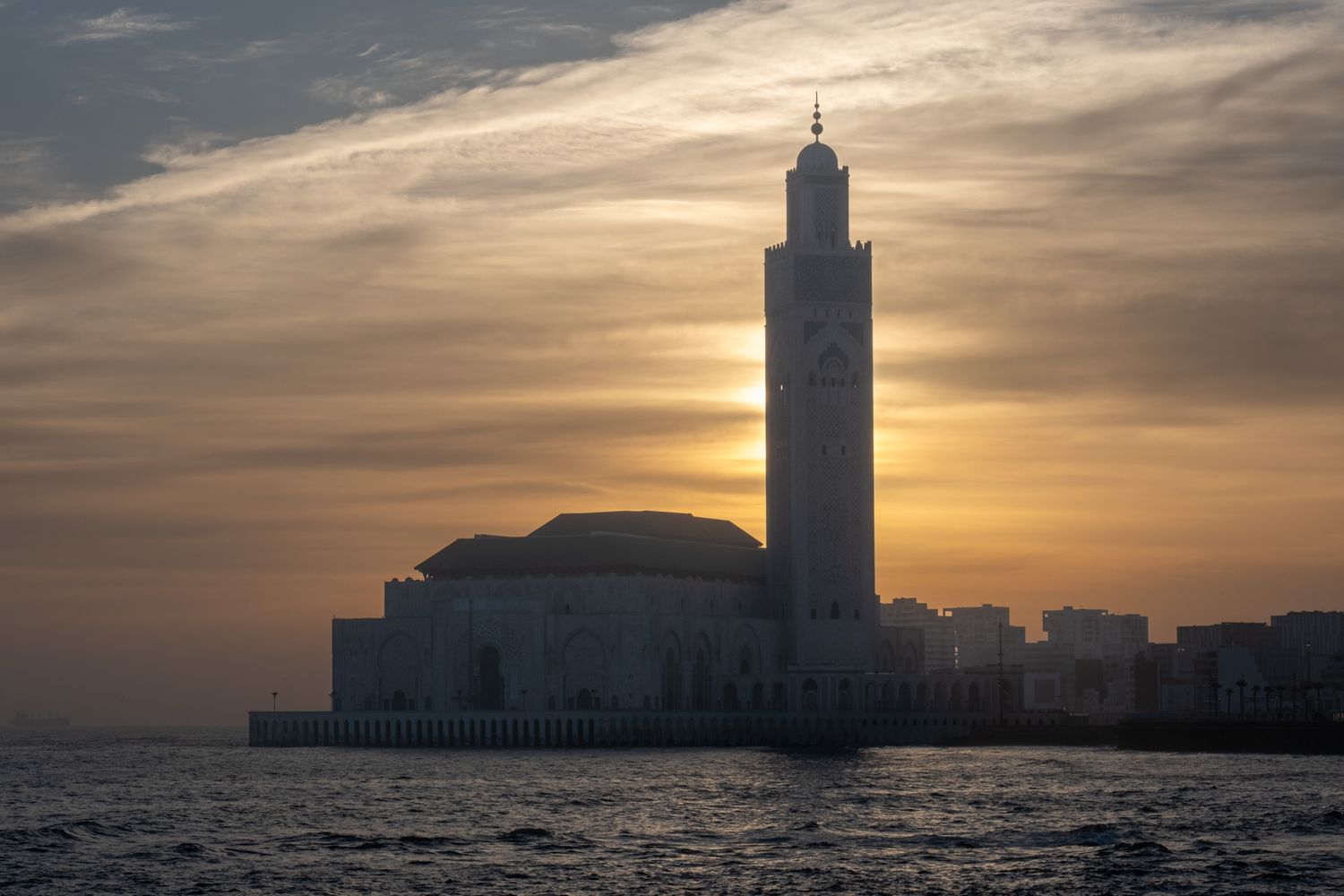 Hassan II Mosque silhouetted against dramatic sunset sky over ocean in Casablanca, Morocco.
