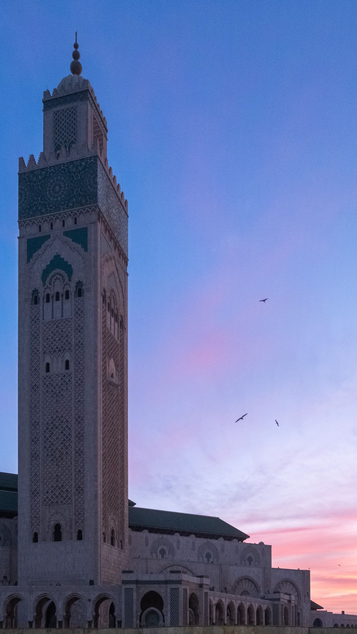 Hassan II Mosque minaret towering against a pink and purple sunset sky in Casablanca.
