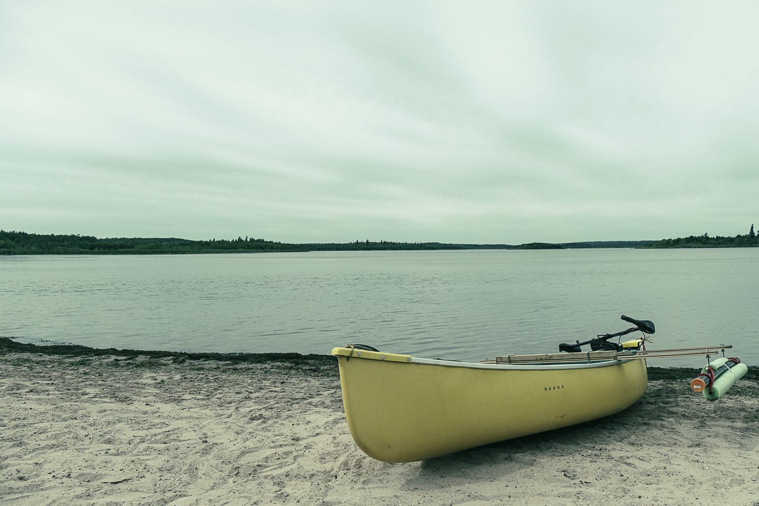 Pale yellow canoe rests on sandy beach shore under overcast sky.