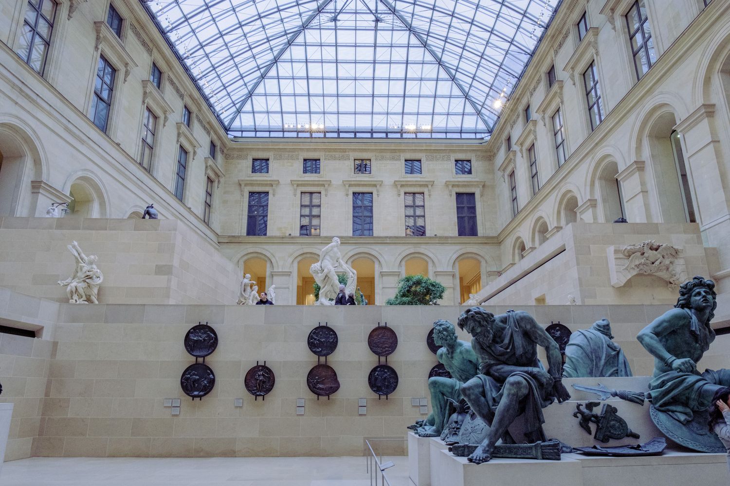 Museum interior with glass ceiling and classical sculptures displayed along white walls.