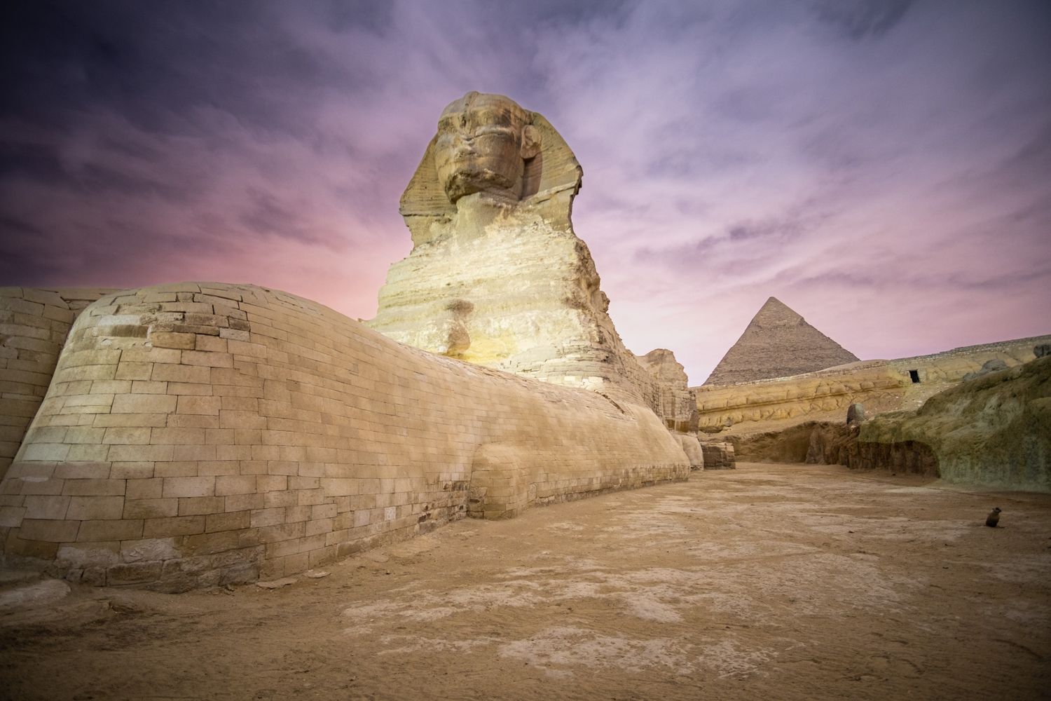 Great Sphinx of Giza and pyramid silhouetted against dramatic purple sky at dusk.