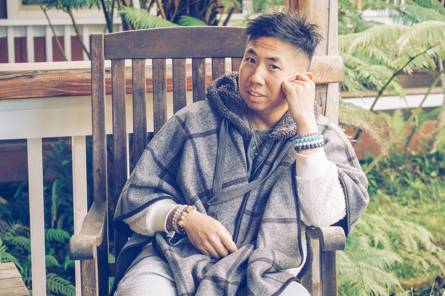 Person relaxing in casual attire on a wooden bench surrounded by tropical plants.