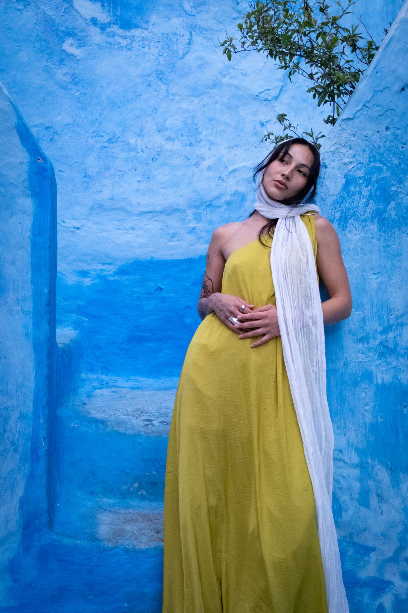 Artistic portrait against vibrant blue walls in Morocco featuring a yellow maxi dress and white scarf.