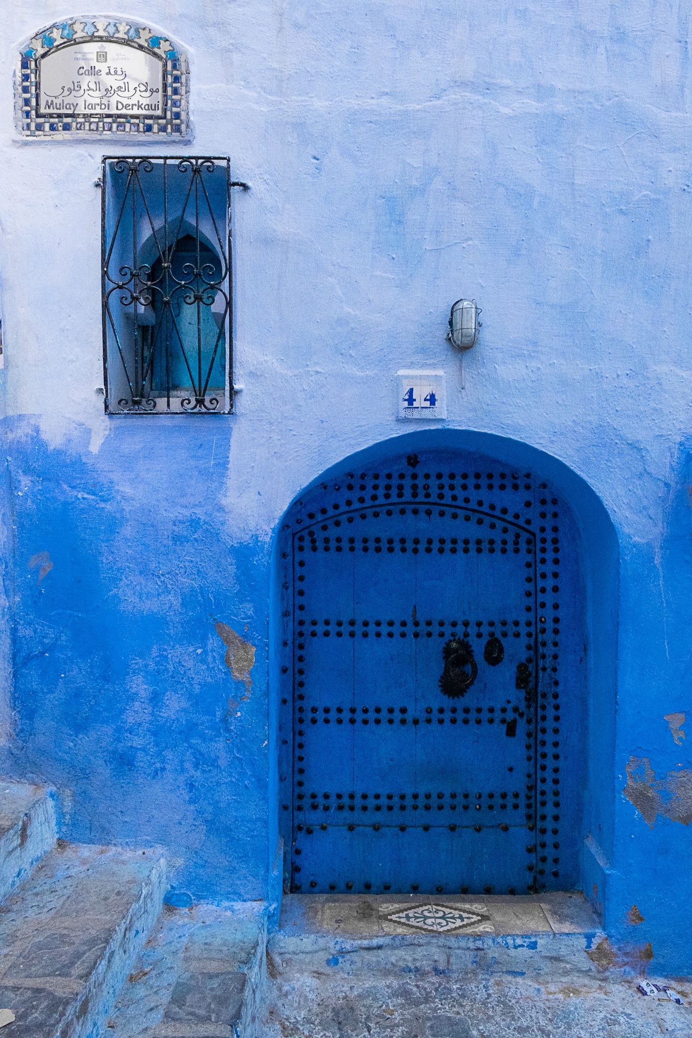 Traditional blue Moroccan door and window against gradient blue wall in Chefchaouen.