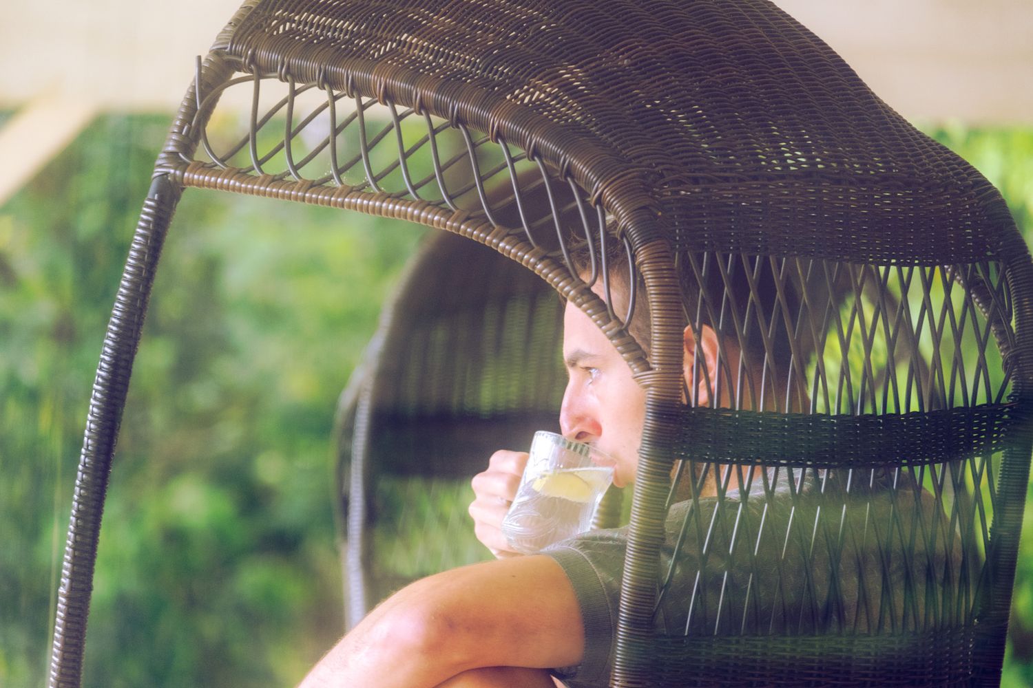 Figure relaxing in wicker chair under vintage-style canopy.
