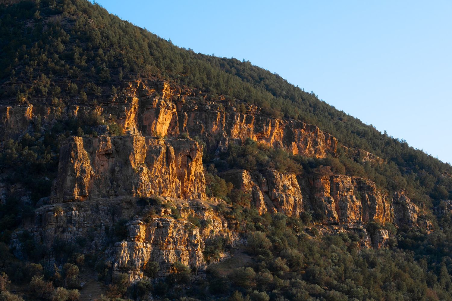 Golden cliffs and rocky outcrops illuminate a mountainside during sunset creating dramatic natural lighting.