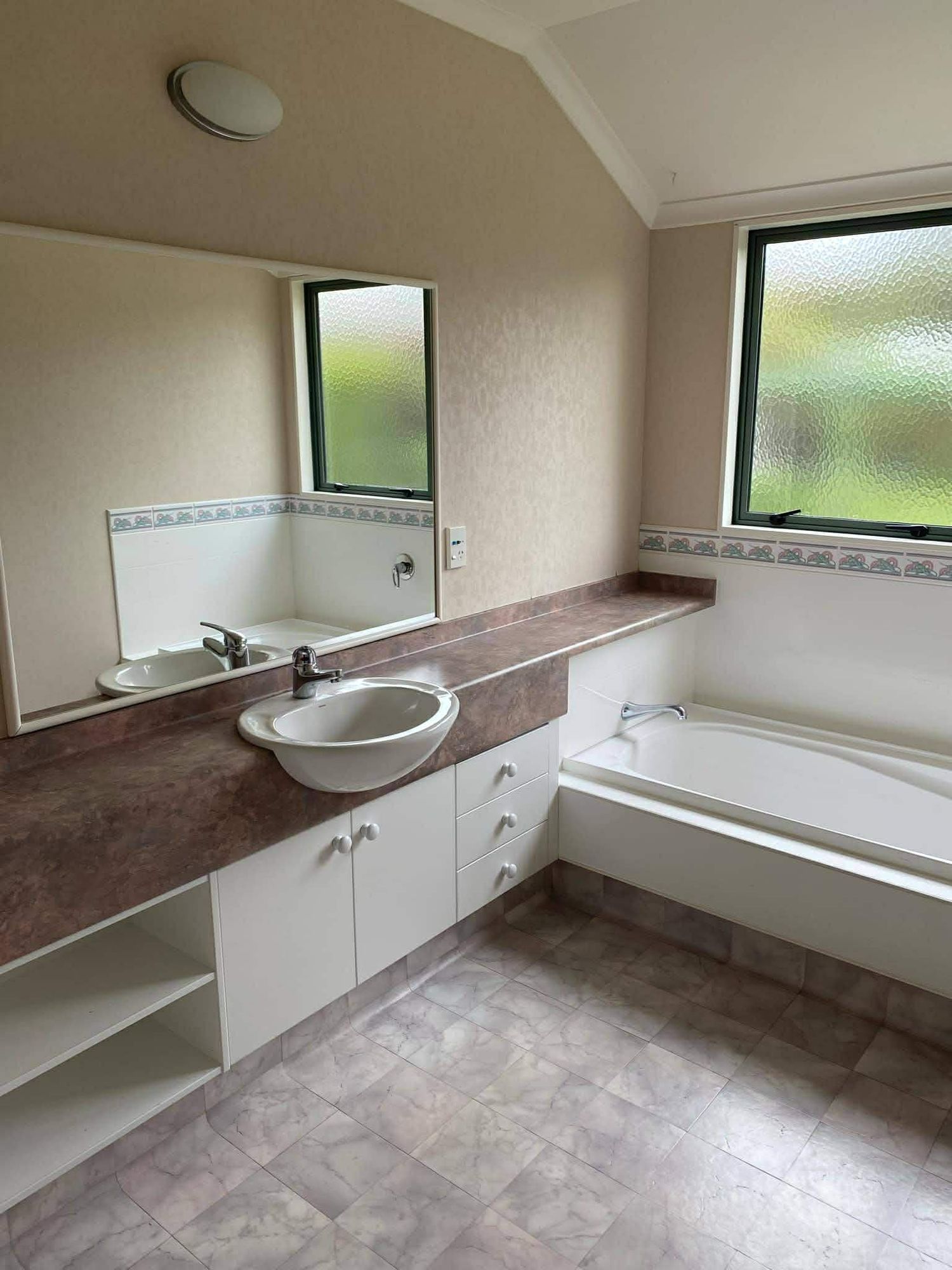 Modern bathroom with white cabinets, brown countertop, and high windows under construction.