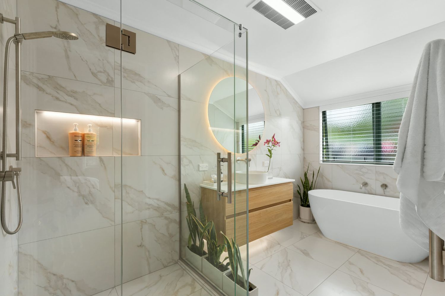 Elegant white marble bathroom with walk-in shower, wood accents, and natural lighting.