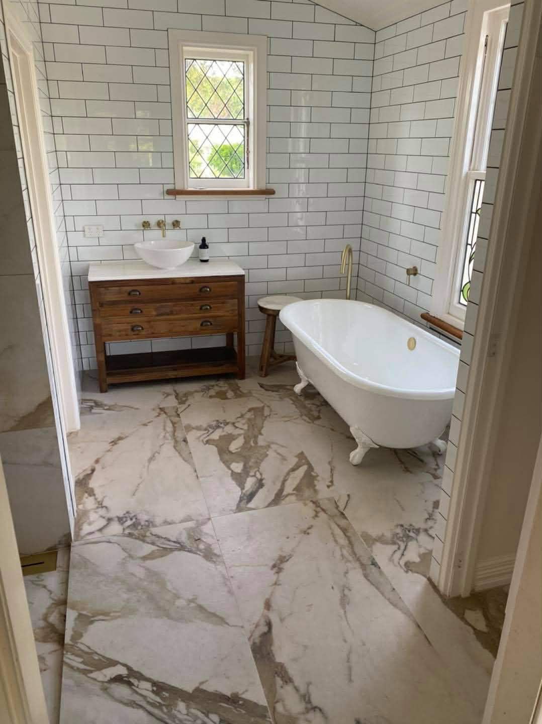 Luxury bathroom featuring marble floors, freestanding tub, and white subway tile walls.