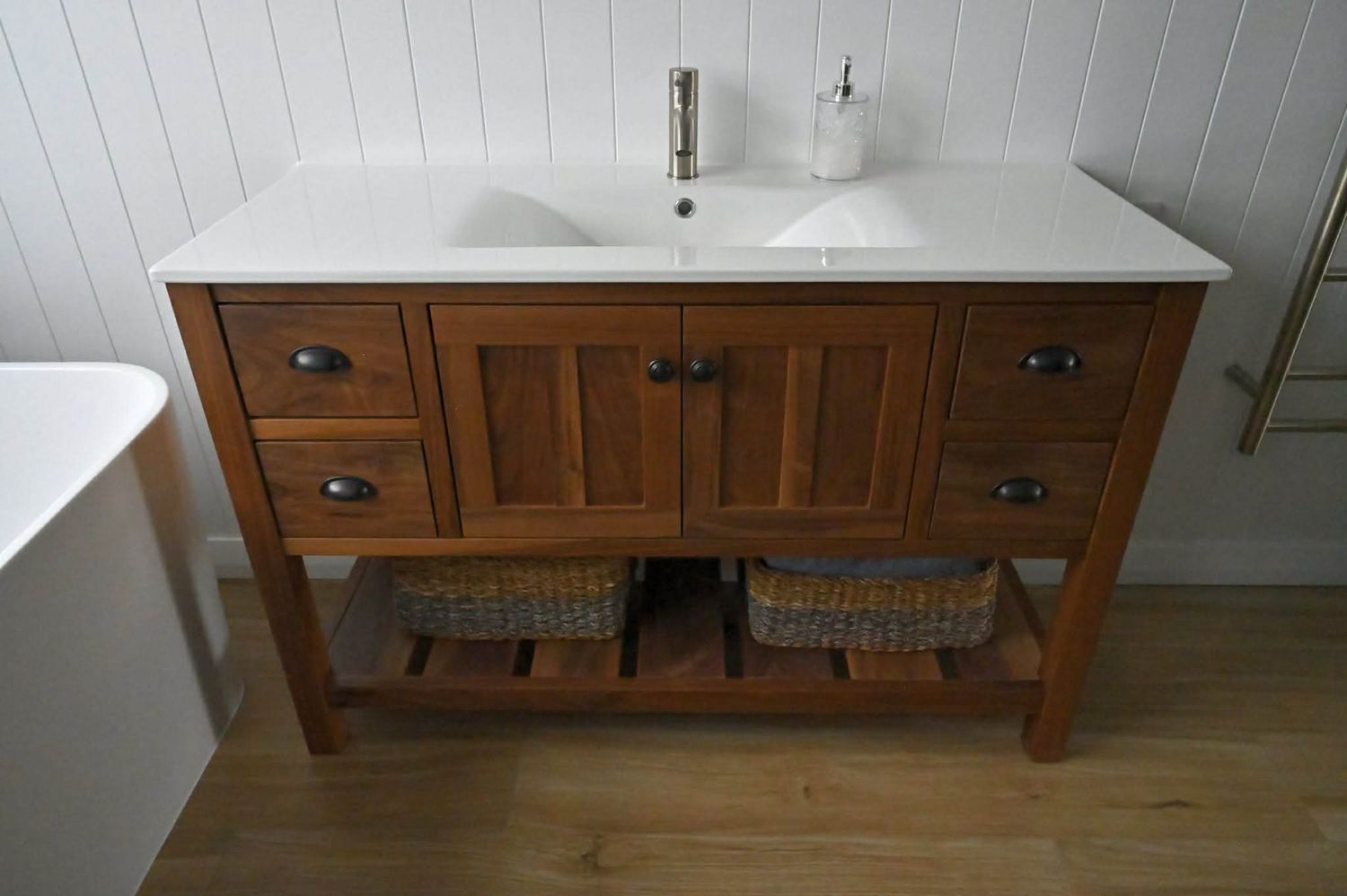 Custom wooden bathroom vanity with white countertop and drawers mounted along a white wall.