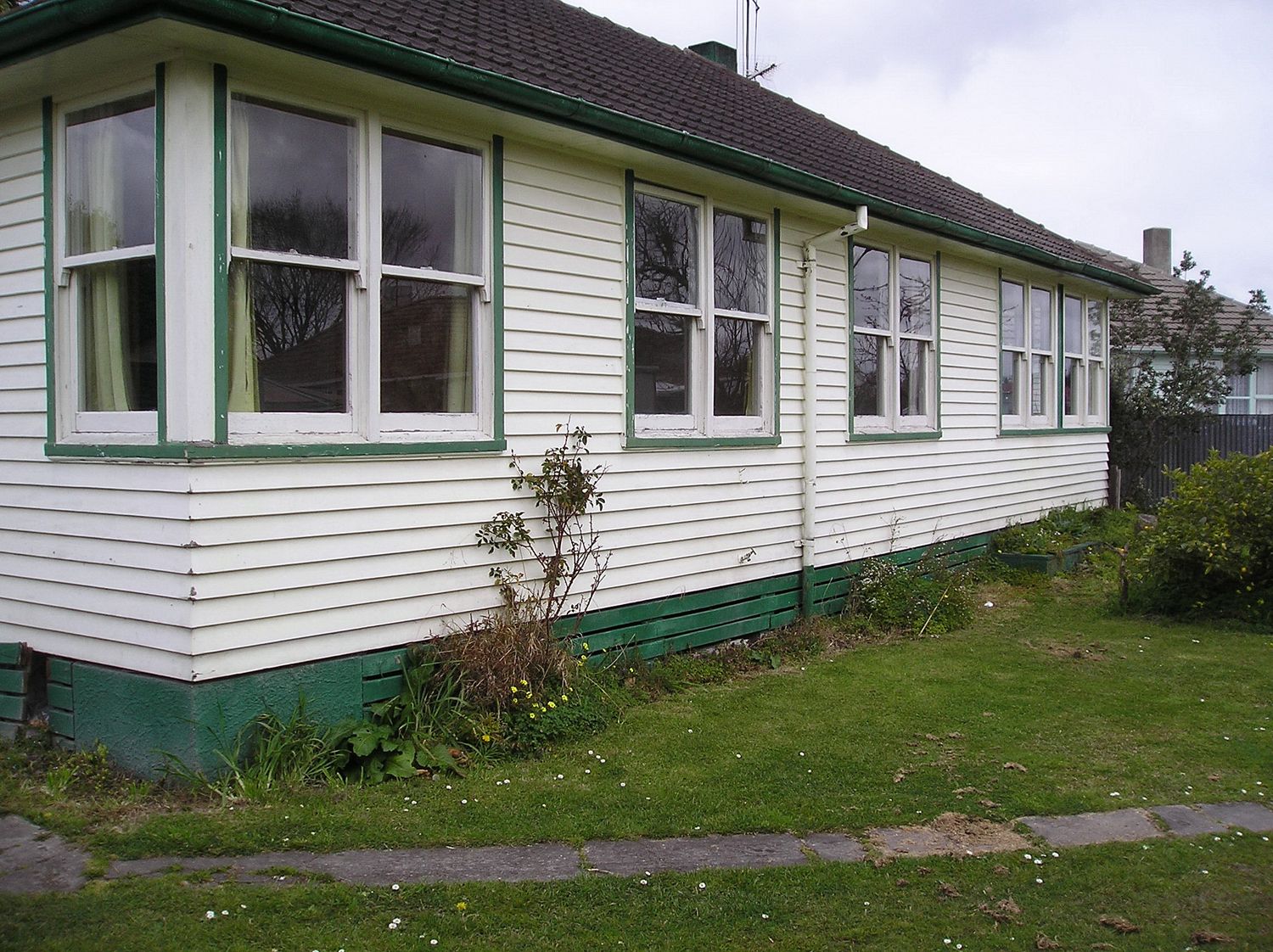 Panoramic view of a white weatherboard house exterior with green trim and multiple windows.