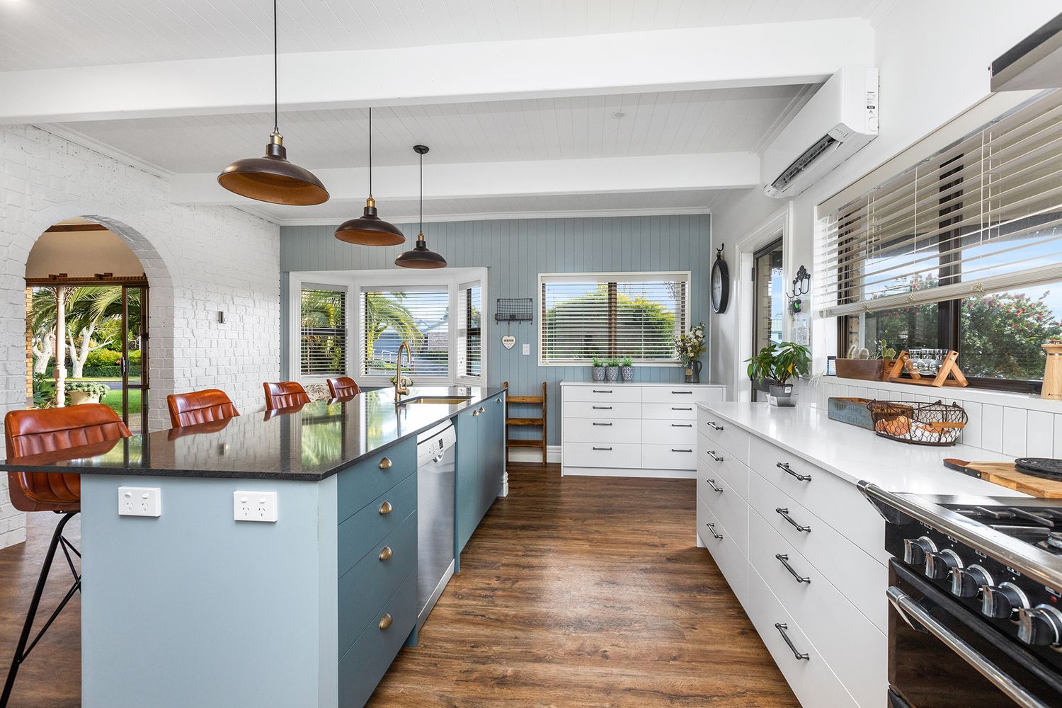 Modern white kitchen with copper pendant lights, hardwood floors and bar seating along a sleek island counter.