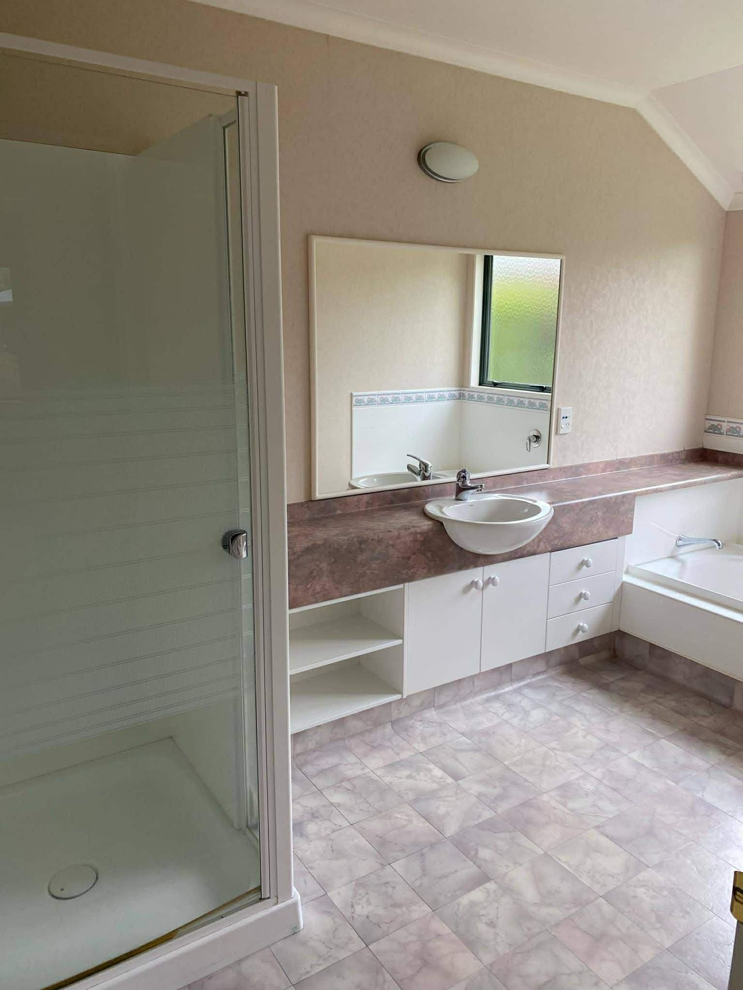 Spacious bathroom interior with glass shower enclosure, white cabinetry and tiled flooring.