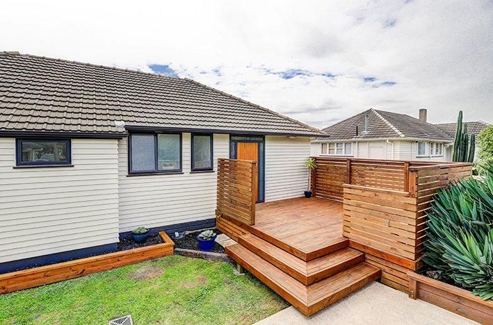 Modern house exterior featuring new wooden deck with steps and contemporary railing.