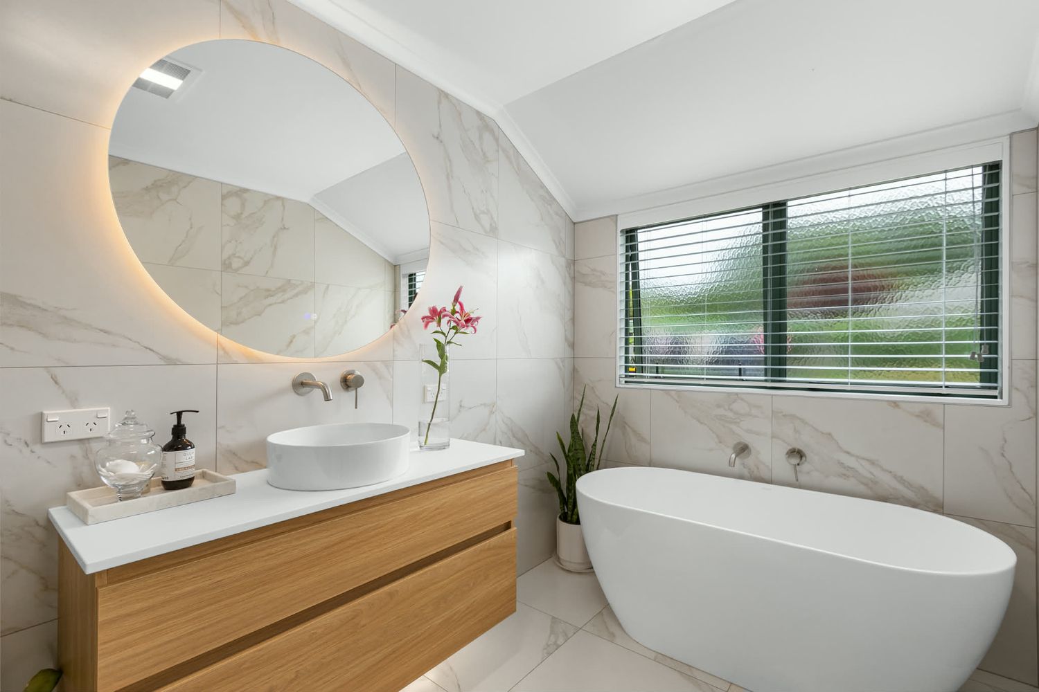 Luxurious marble bathroom featuring freestanding tub, wooden vanity, and ambient lighting.