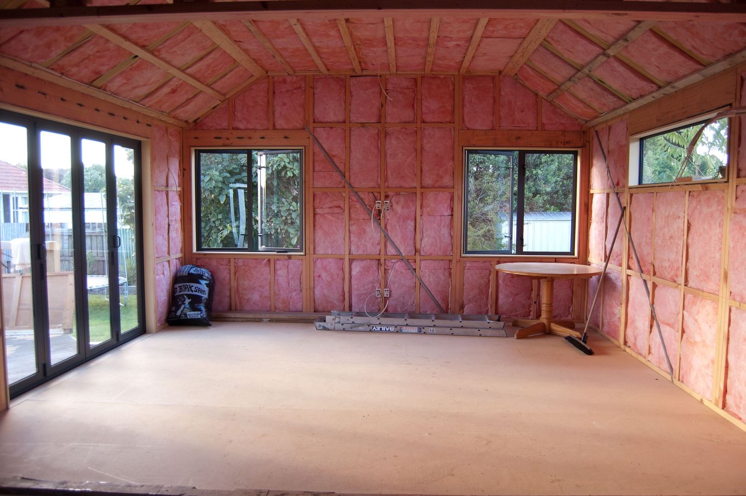Large unfinished room with exposed pink insulation and multiple windows.