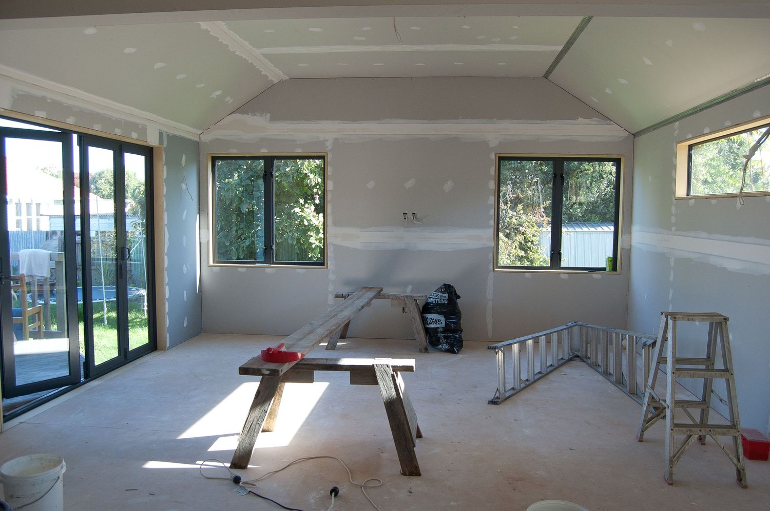 Spacious room under construction with fresh drywall and large windows letting in natural light.