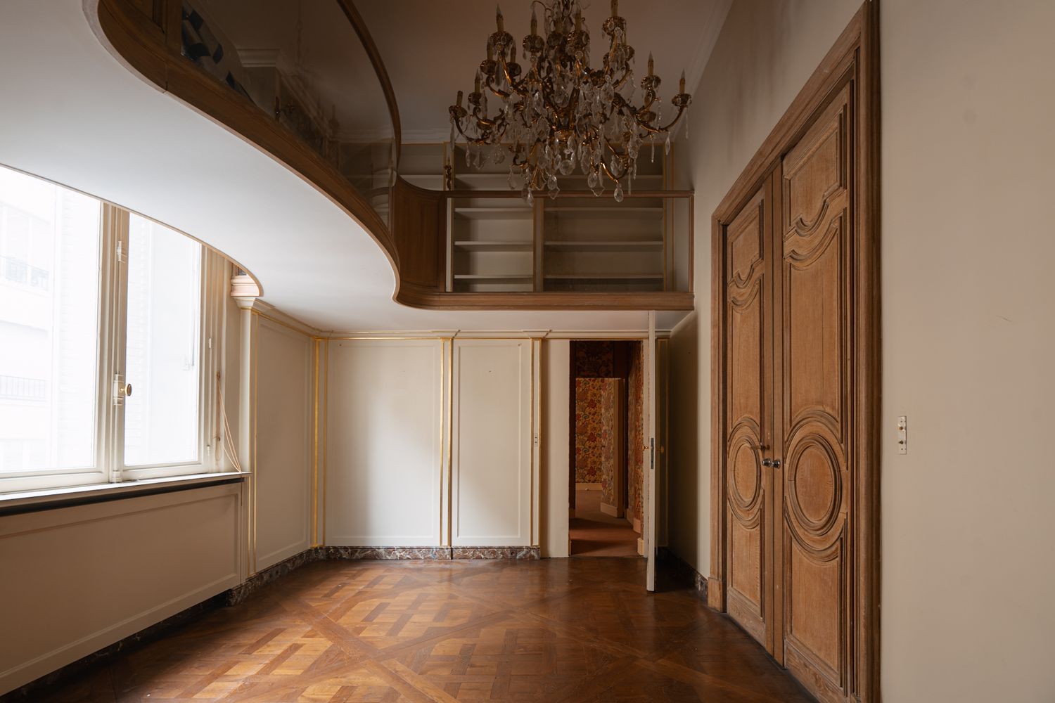 Empty luxurious room interior with herringbone wood floor, ornate molding, and crystal chandelier pendant light.