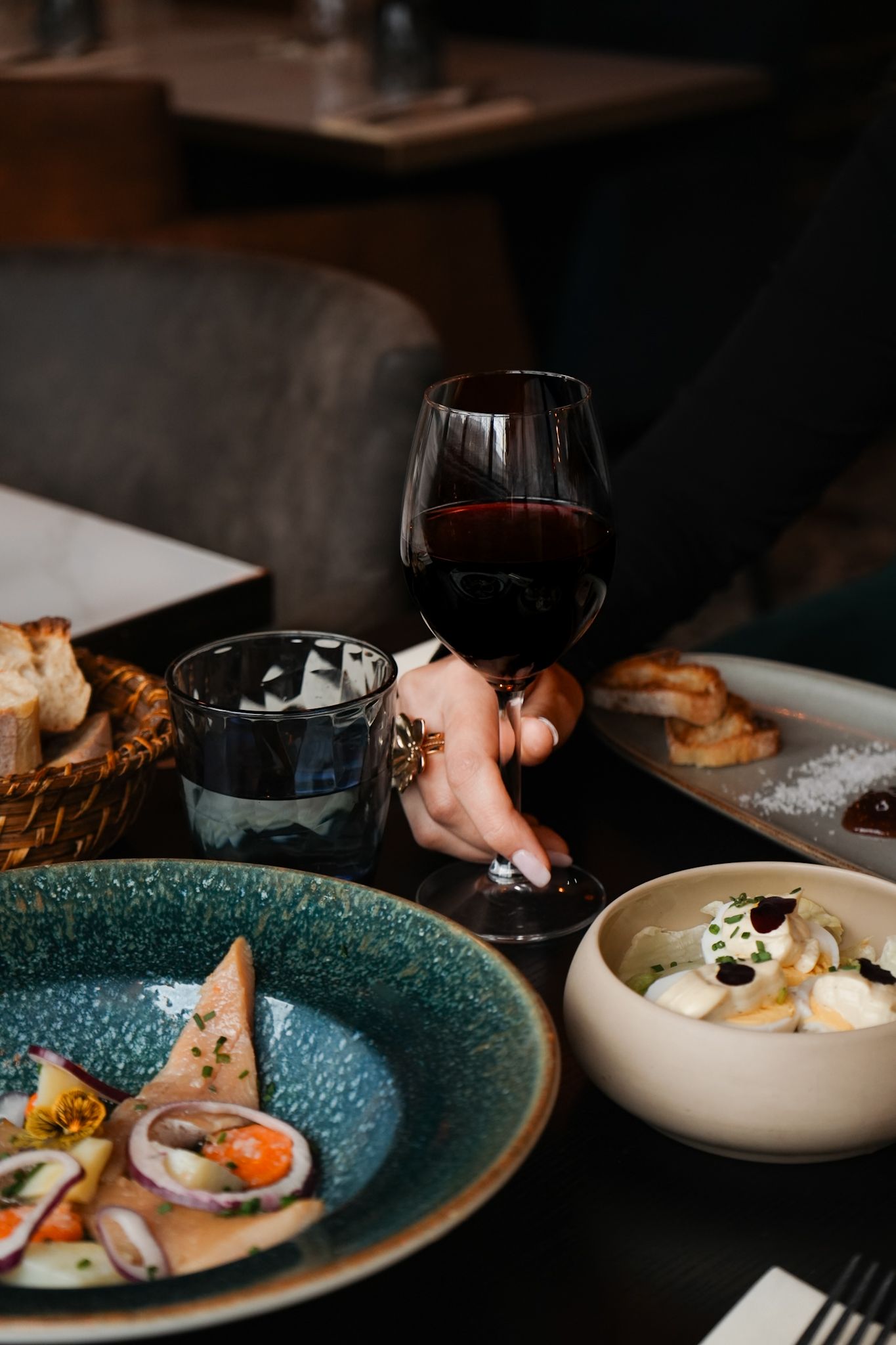 Wine glass held by a diner at restaurant table with seafood plates and bread on dark table setting.