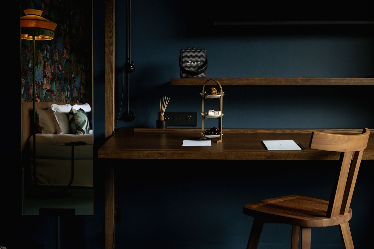 A dark moody desk setup with a wooden chair and coffee grinder in a dimly lit room with blue walls.