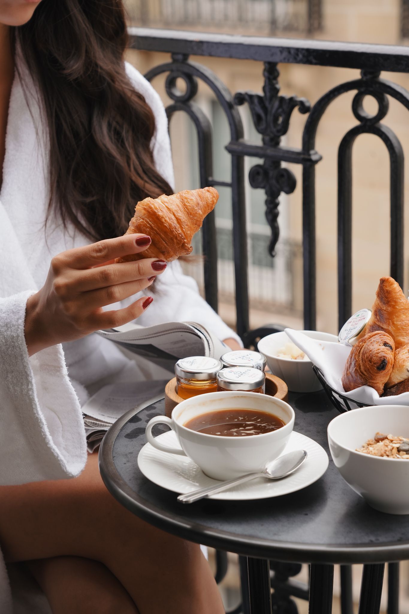 Breakfast setting on a Parisian balcony with croissants, hot chocolate and elegant tableware.