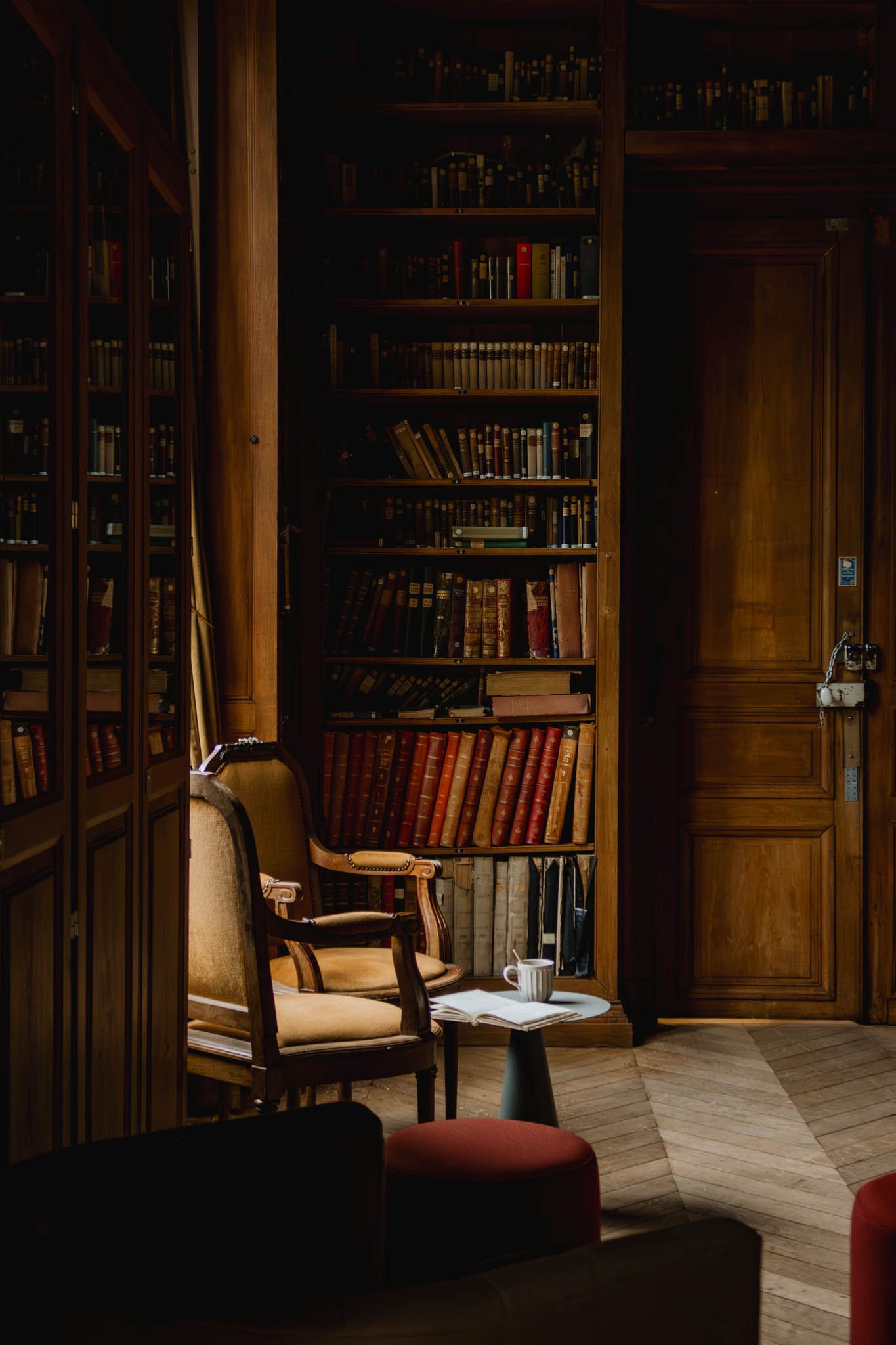 A cozy reading nook with a vintage armchair and floor-to-ceiling bookshelves in a warm, wood-paneled library.