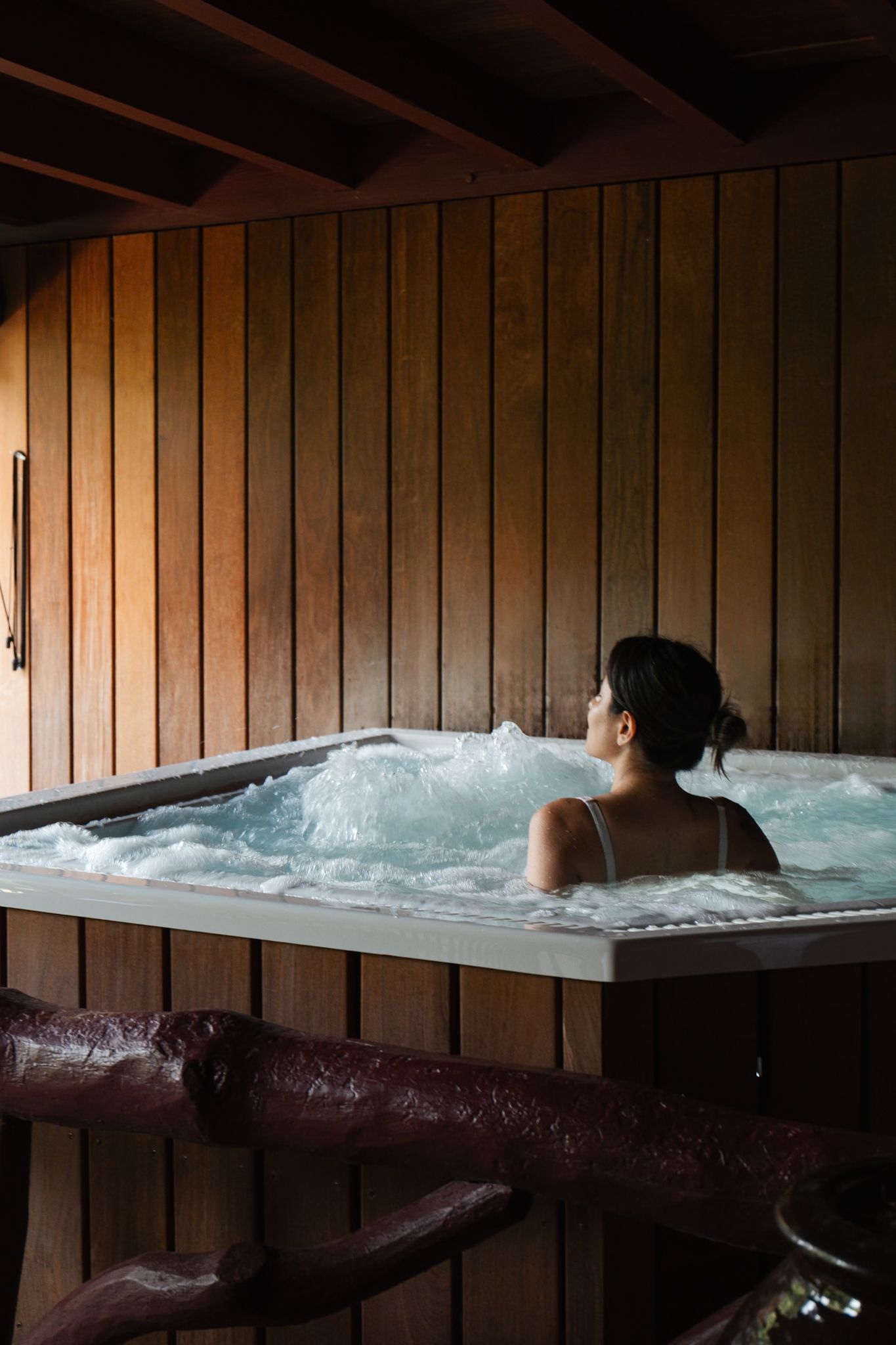 Person relaxing in an outdoor hot tub with wooden walls at dusk creating a cozy spa atmosphere.